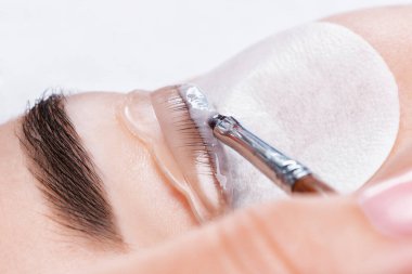 Makyöz, güzellik salonunda güzel bir kadına kirpik boyama ve kaplama prosedürünü uyguluyor. Kirpik uzantıları. Kirpikleri yakın çekim.