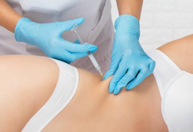 Estetik kozmetik uzmanı bir kadının vücudunda yağ yakmak için lipolitik enjeksiyon yapar. Güzellik salonunda kadın estetiği. Kozmetoloji konsepti..