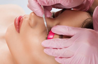 Makyöz, güzellik salonunda güzel bir kadına kirpik boyama ve kaplama prosedürünü uyguluyor. Kirpik uzantıları. Kirpikleri yakın çekim.