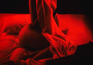 Genç bir webcam mankeni dizüstü bilgisayarın önünde oturuyor. Yatak odasındaki beyaz bir yatakta iletişim kuruyor..