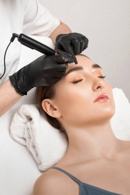 Güzellik salonunda güzel bir kadının kaşları için kalıcı makyaj. Yakından bir güzellik uzmanı kaş dövmesi yapıyor. Gözlerdeki oklar