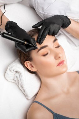 Güzellik salonunda güzel bir kadının kaşları için kalıcı makyaj. Yakından bir güzellik uzmanı kaş dövmesi yapıyor. Gözlerdeki oklar