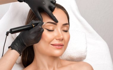 Güzellik salonunda güzel bir kadının kaşları için kalıcı makyaj. Yakından bir güzellik uzmanı kaş dövmesi yapıyor. Gözlerdeki oklar