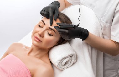 Güzellik salonunda güzel bir kadının kaşları için kalıcı makyaj. Yakından bir güzellik uzmanı kaş dövmesi yapıyor. Gözlerdeki oklar