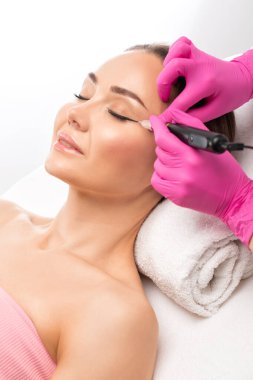 Güzellik salonundaki güzel kadınların kaşları ve dudakları için kalıcı makyaj. Yakından bir güzellik uzmanı kaş dövmesi yapıyor. Gözlerdeki oklar