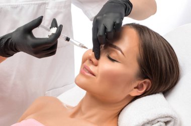 Doktor burundaki kamburu sarışının güzelliğiyle düzeltmek için iğne yapar. Güzellik uzmanı, yüzündeki kırışıklıklara karşı iğne yapar. Güzellik salonunda kadın kozmetolojisi.