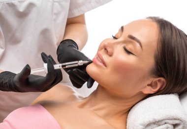 Kozmetik uzmanı, güzel bir kadının burun kıvrımlarında dudak büyütme ve kırışıklık önleyici iğneler yapar. Güzellik salonunda kadın kozmetolojisi.