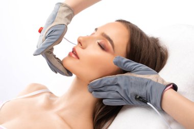 Bir kozmetolog, güzellik salonunda genç ve güzel bir kızın yüzüne ve boynuna mikro akım masaj uygular..