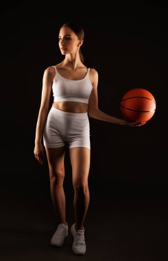 Beyaz şortlu güzel, atletik sarışın bir kız ve bir top neon ışıklı siyah bir arka planda basketbol oynuyor..