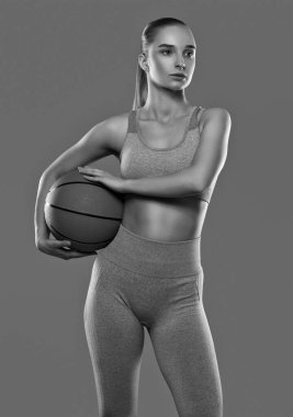 Mor spor takım elbiseli güzel bir sarışın kız pembe bir arka planda basketbol oynuyor..