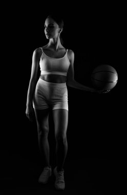 Beyaz şortlu güzel, atletik sarışın bir kız ve bir top neon ışıklı siyah bir arka planda basketbol oynuyor..