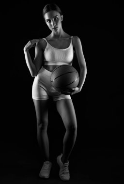 Beyaz şortlu güzel, atletik sarışın bir kız ve bir top neon ışıklı siyah bir arka planda basketbol oynuyor..