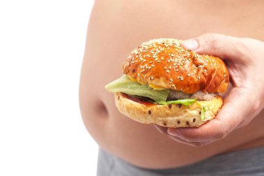 Karnının yanında hamburger tutan ve göbeğini gösteren şişman bir adam. Sağlıksız yemek kavramı.