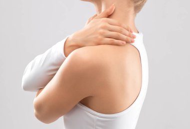 İzole edilmiş beyaz elbiseli ince bir kadın. Kendine omuz ve boyun masajı yapıyor. Sağlıklı yaşam tarzı, spor ve diyet.