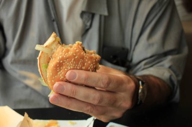 Elinde taze yapılmış bir hamburger tutan adam.