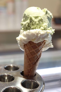 Taze kepçelenmiş dondurma külahı. Metal bir büfede çeşitli tatlar sergileniyor.