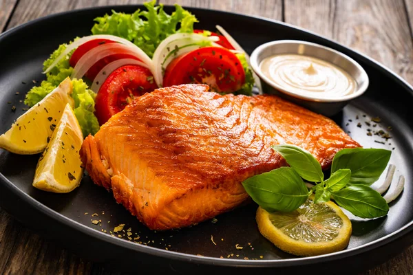 Seared salmon steaks with lettuce, tomatoes and lemons on wooden table