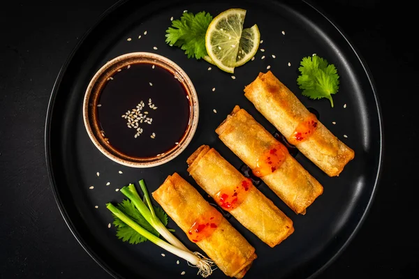 Vegetable filled spring rolls and soy sauce on black wooden table