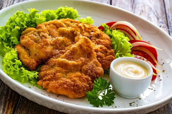 Crispy breaded seared chicken cutlet with lettuce and tomatoes on wooden table