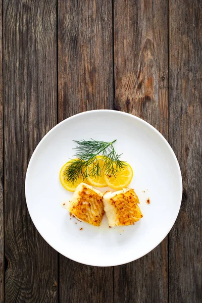 烤鳕鱼卷和切片柠檬放在木制桌子上 — 图库照片