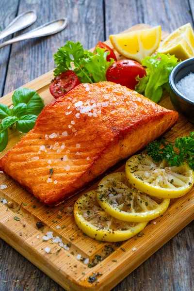 Seared salmon steak with lettuce, tomatoes and lemon on wooden table