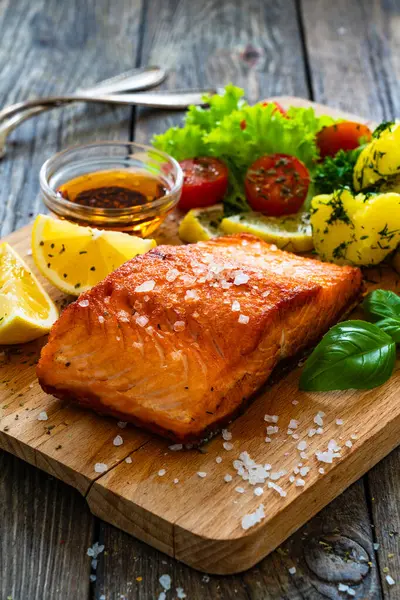 Seared salmon steak with lettuce, tomatoes and boiled potatoes on wooden table