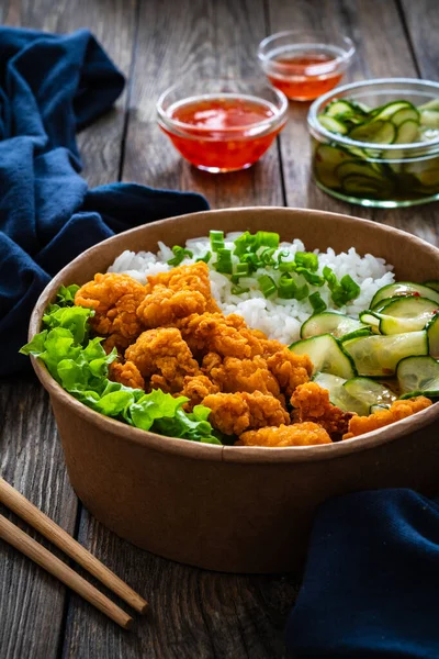 Korean fried chicken - seared breaded chicken nuggets served with white rice and vegetables on wooden table
