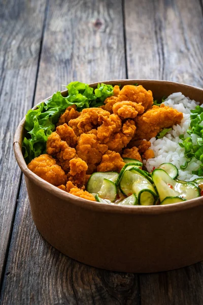 Korean fried chicken - seared breaded chicken nuggets served with white rice and vegetables on wooden table