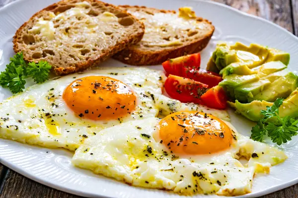 Breakfast - sunny side up egg, toasted bread and avocado served on wooden table