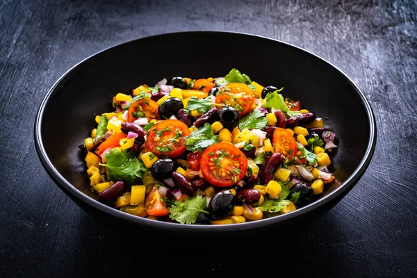 Mexican style salad - red beans, black olives, corn, yellow pepper, onion and tomatoes on wooden table
