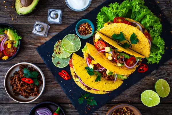Tacos with ground beef, avocado, corn and fresh vegetables on wooden table