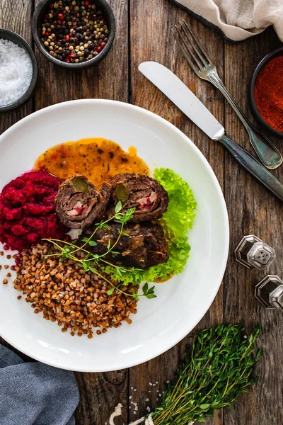 Wrapped beef in sauce served with boiled buckwheat and grated beets on wooden table
