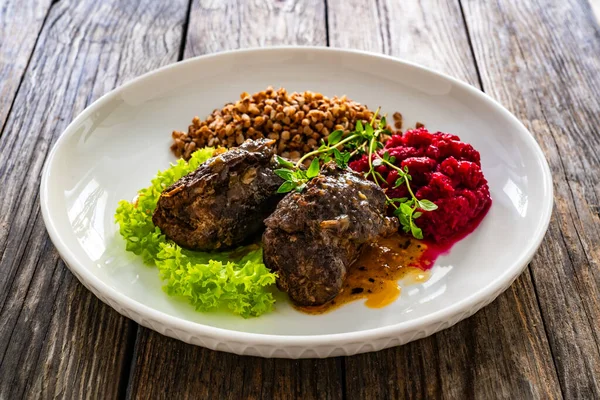 Wrapped beef in sauce served with boiled buckwheat and grated beets on wooden table
