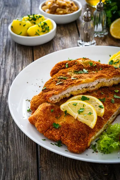 Crispy breaded fried cutlet with boiled potatoes and cooked cabbage on wooden table
