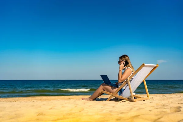在海滩上使用笔记本电脑和智能手机的中年女性 — 图库照片
