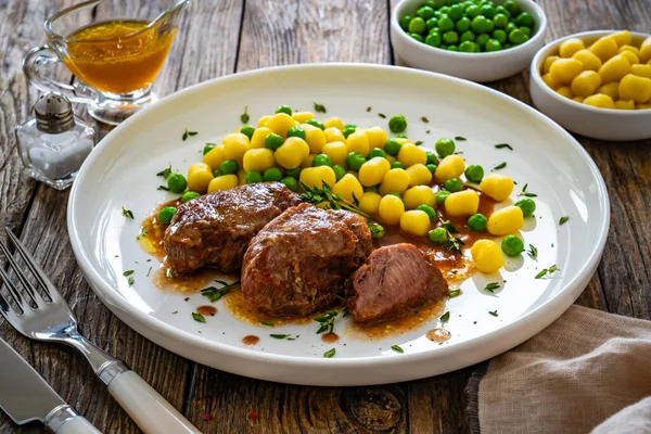 Baked pork cheeks in sauce with gnocchi and green peas on wooden table