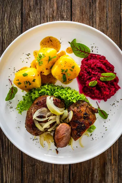 Baked pork cheeks with boiled potatoes and beetroots on wooden table