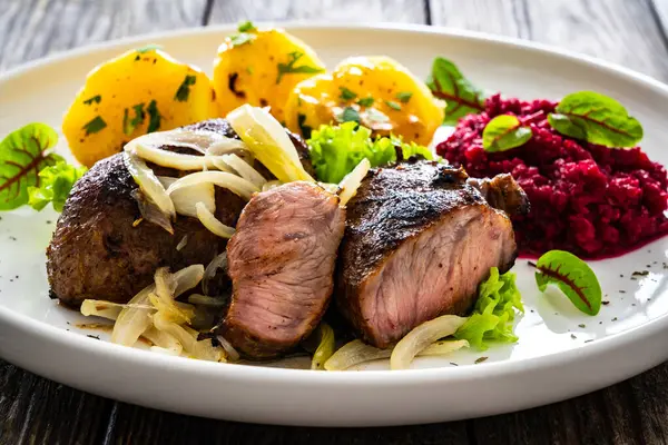 Baked pork cheeks with boiled potatoes and beetroots on wooden table
