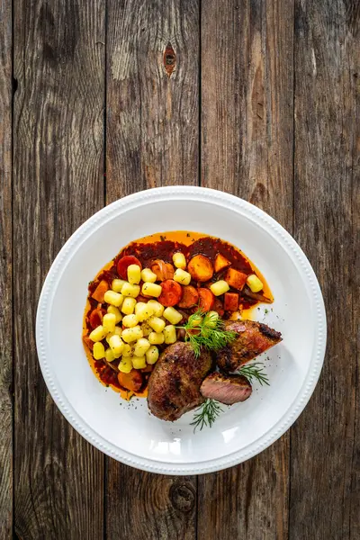 Baked pork cheeks with gnocchi and boiled vegetables in sauce on wooden table