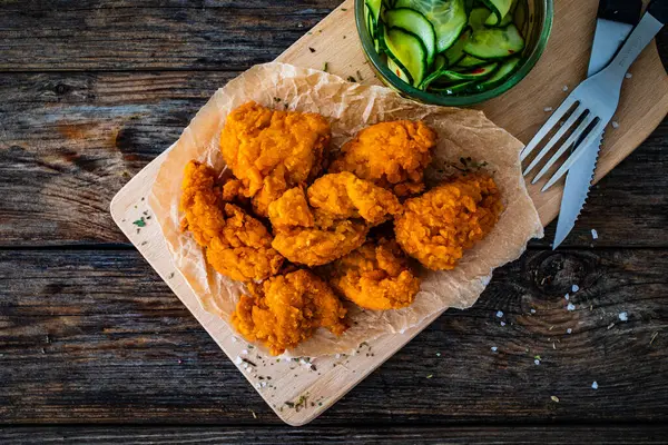 Fried breaded chicken nuggets served with fresh vegetables on wooden table
