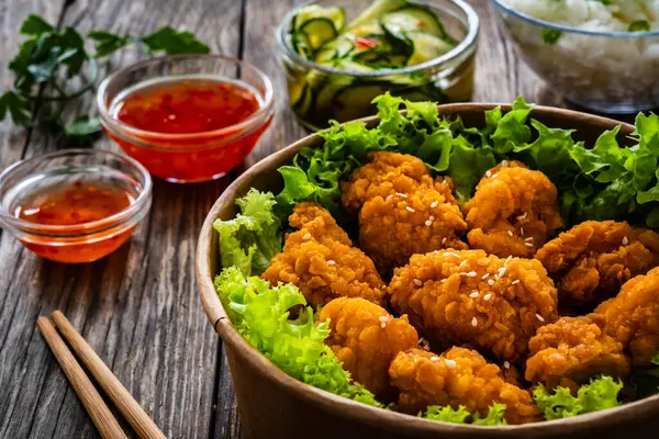 Takeaway food - fried breaded chicken nuggets and vegetables on wooden table
