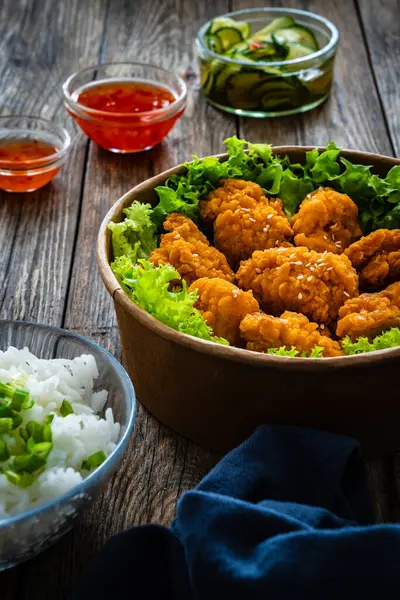 Takeaway food - fried breaded chicken nuggets and vegetables on wooden table