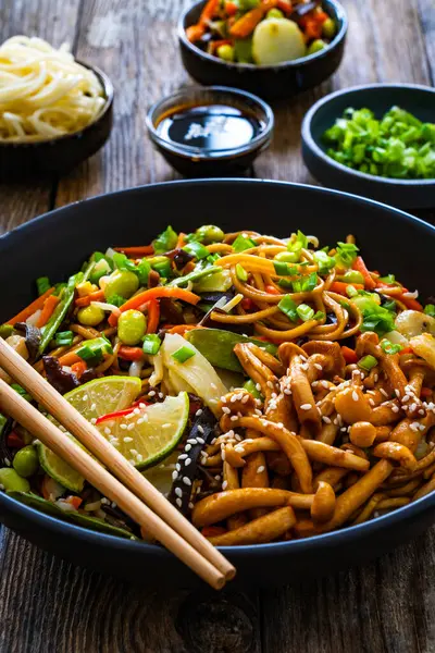 アジアスタイルの炒め野菜と麺を木のテーブルに ロイヤリティフリーのストック画像