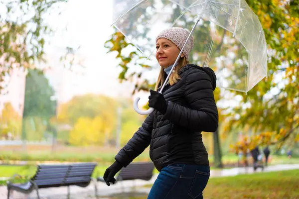 健康的生活方式 中年妇女手持雨伞在城市公园散步 图库图片