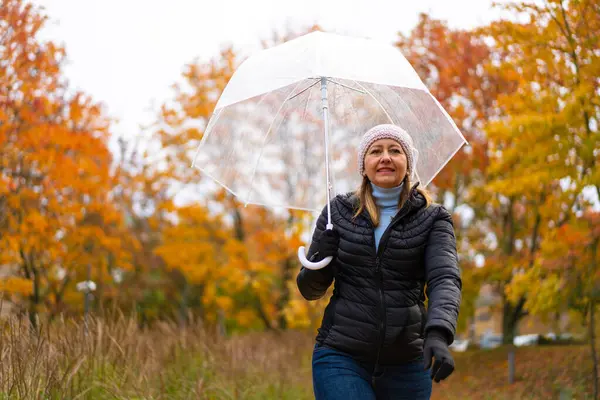 健康的生活方式 中年妇女手持雨伞在城市公园散步 图库照片