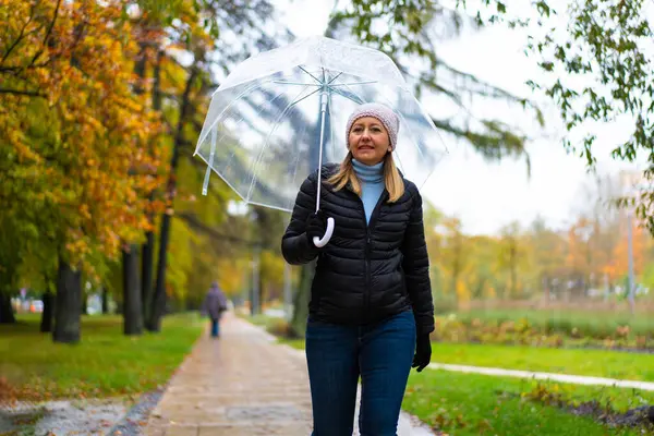 健康的生活方式 中年妇女手持雨伞在城市公园散步 图库图片