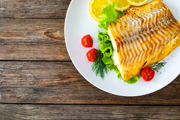 stock image Fried cod loin and fresh vegetables on wooden table 