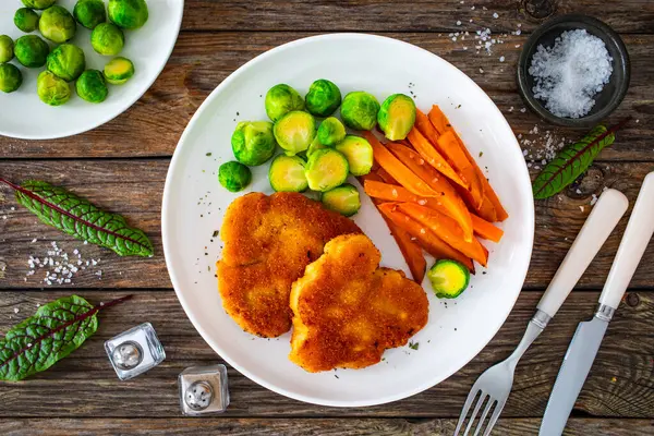 Crispy breaded fried pork loin chops with sweet potato fries and boiled Brussels sprouts on wooden table