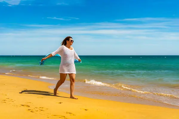 美丽的女人抱着披肩走在阳光灿烂的海滩上 — 图库照片