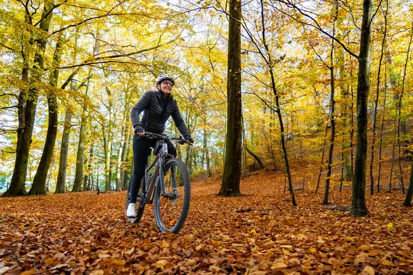 Woman riding bicycle in city forest in autumnal scenery